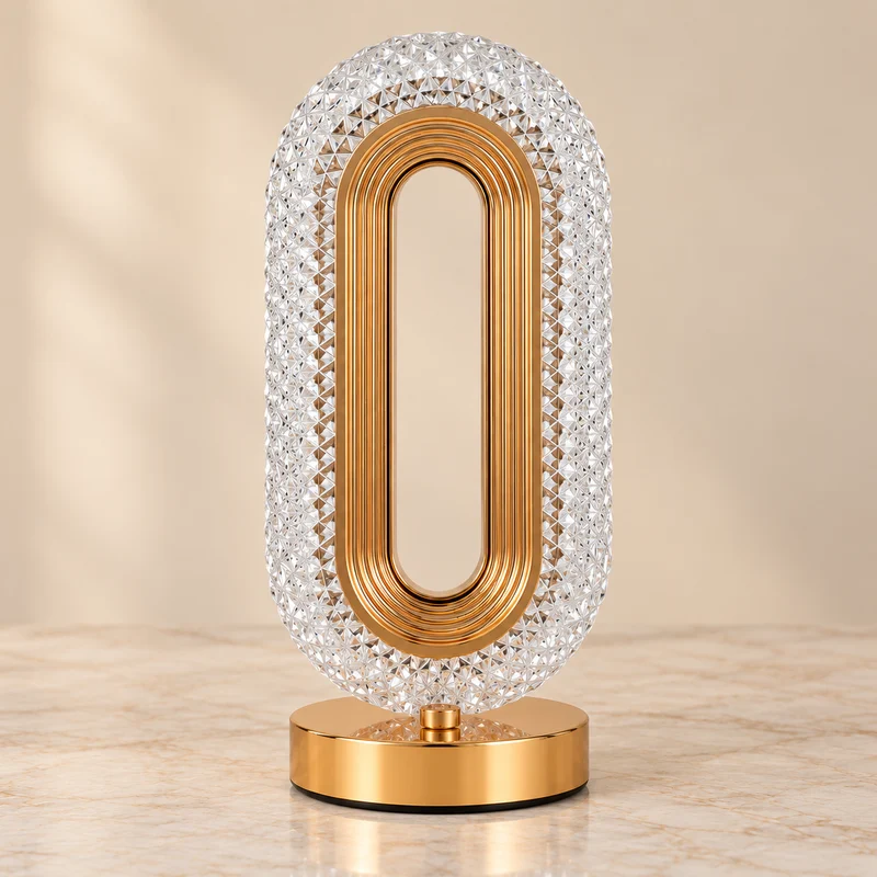 The lamp switched off, showing the clear faceted acrylic shade, ridged gold-tone inner rim and polished base